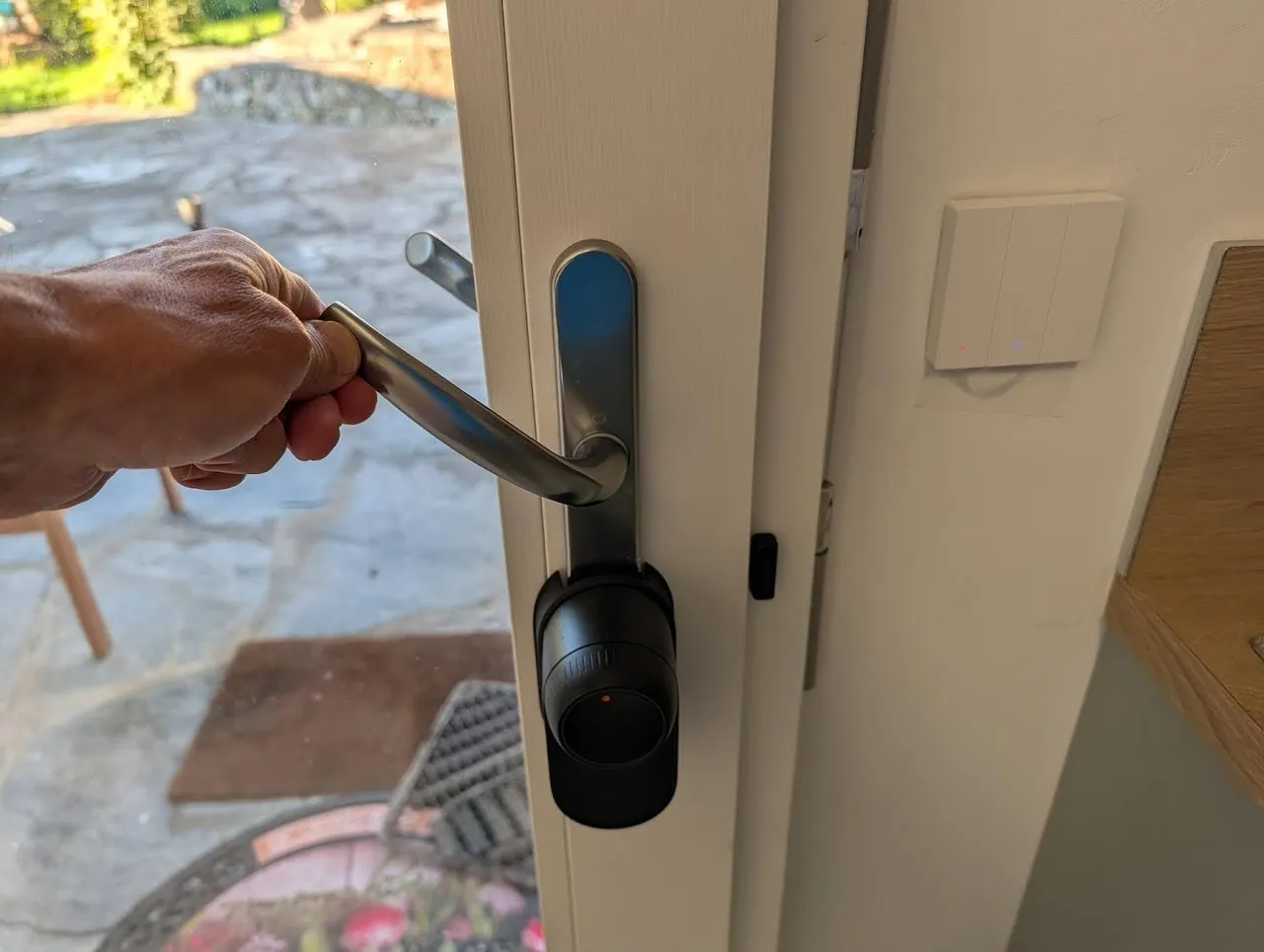 A hand firmly lifting the front door's handle to actuate the deadbolts, with the keypad visible on the door frame.